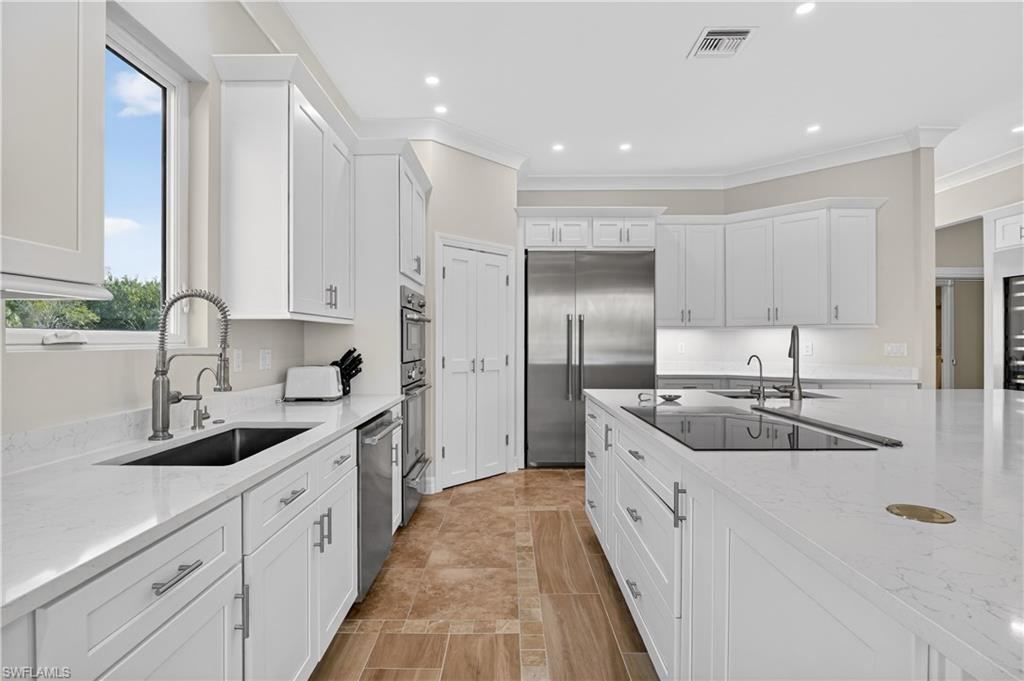 Kitchen featuring white cabinetry, appliances with stainless steel finishes, light stone counters, recessed lighting, and ornamental molding