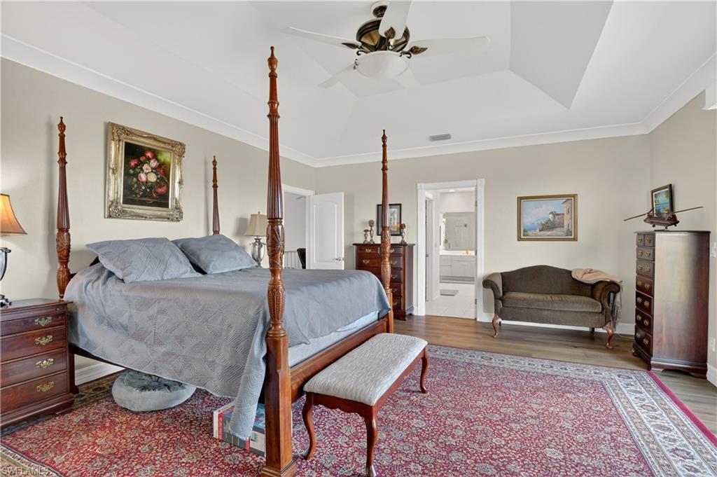Bedroom featuring crown molding, wood finished floors, a ceiling fan, a tray ceiling, and ensuite bathroom