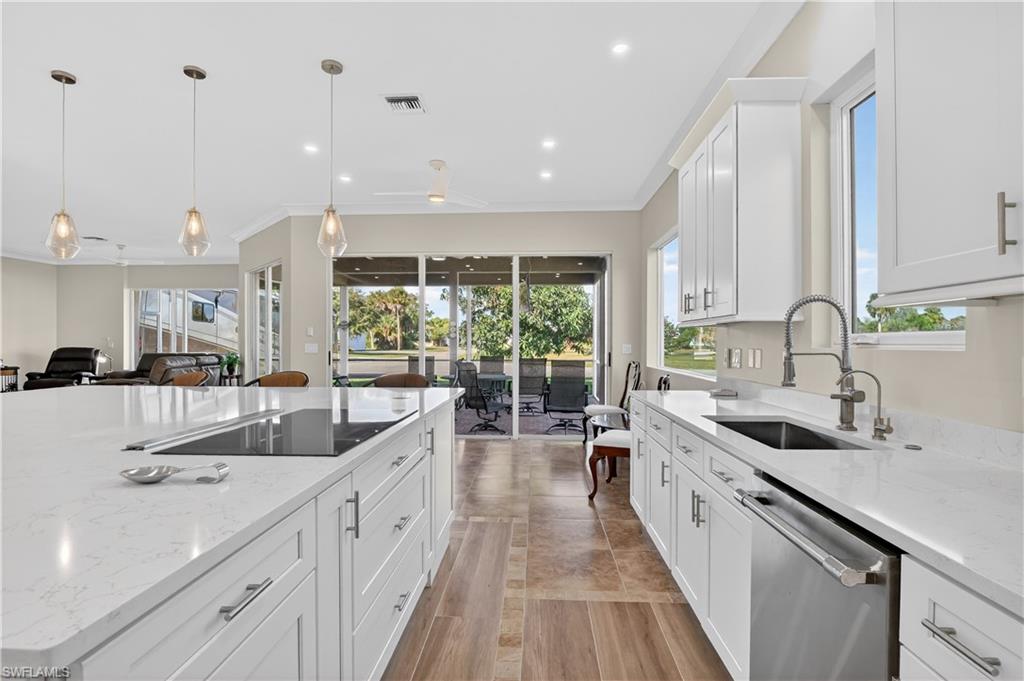 Kitchen with white cabinets, light stone countertops, stainless steel dishwasher, pendant lighting, and open floor plan