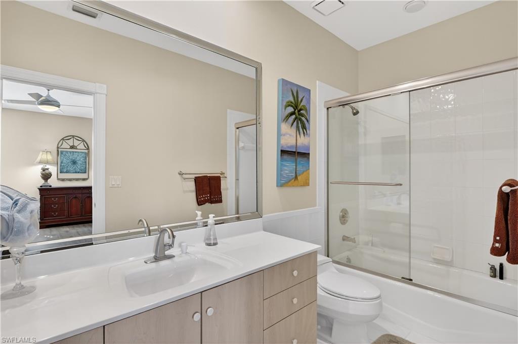 Bathroom featuring connected bathroom, combined bath / shower with glass door, vanity, and a wainscoted wall