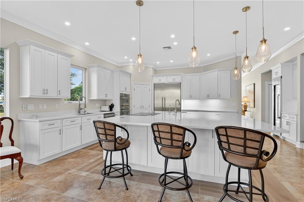 Kitchen with white cabinetry, appliances with stainless steel finishes, a breakfast bar area, a spacious island, and pendant lighting