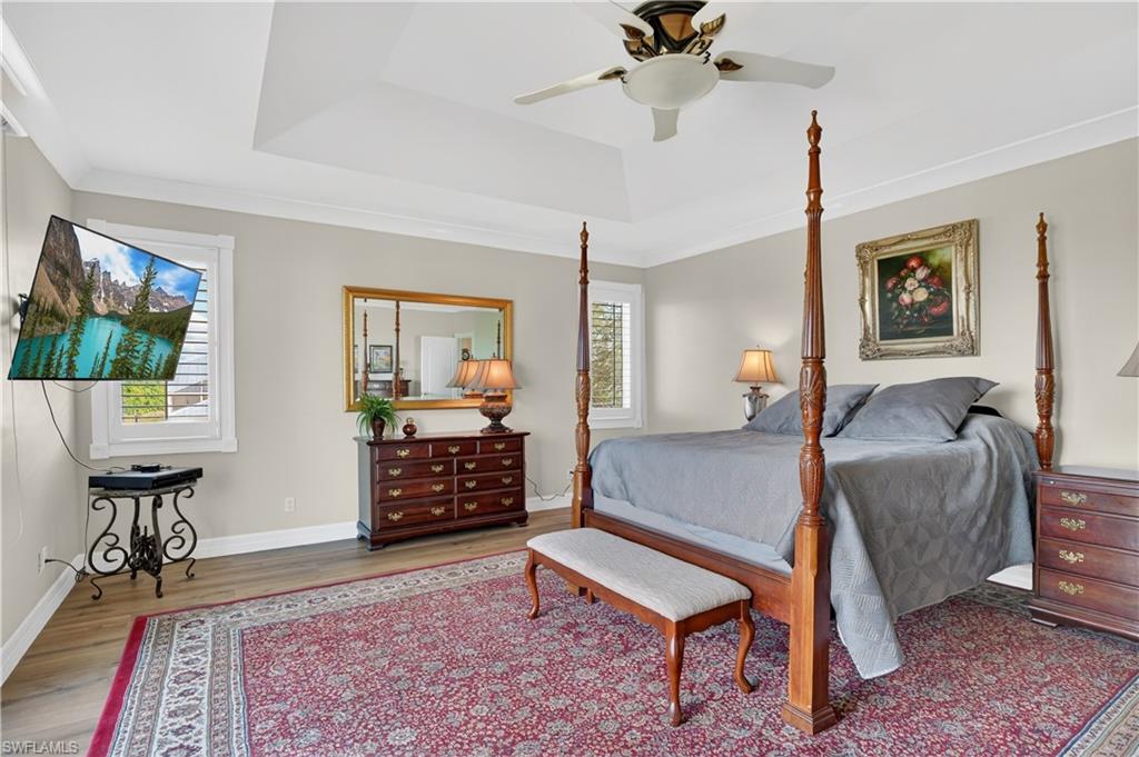 Bedroom with wood finished floors, a ceiling fan, a tray ceiling, and ornamental molding
