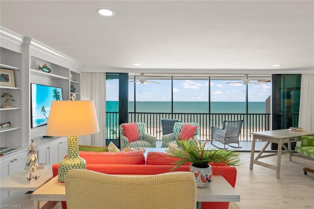 Living area featuring floor-to-ceiling sliding glass doors, light wood-finish flooring, a built-in wall unit with display shelving, recessed lighting, and direct access to an outdoor balcony with water views