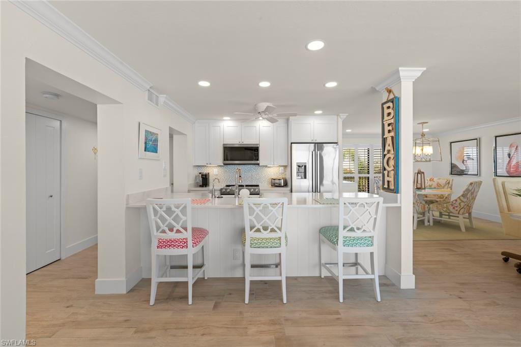 Kitchen featuring white cabinetry, stainless steel appliances, a breakfast bar, recessed lighting, and wood-finish flooring