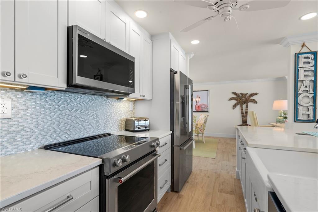 Modern kitchen featuring white shaker cabinetry, stainless steel appliances, a light-toned mosaic tile backsplash, white countertops, and wood-finish flooring