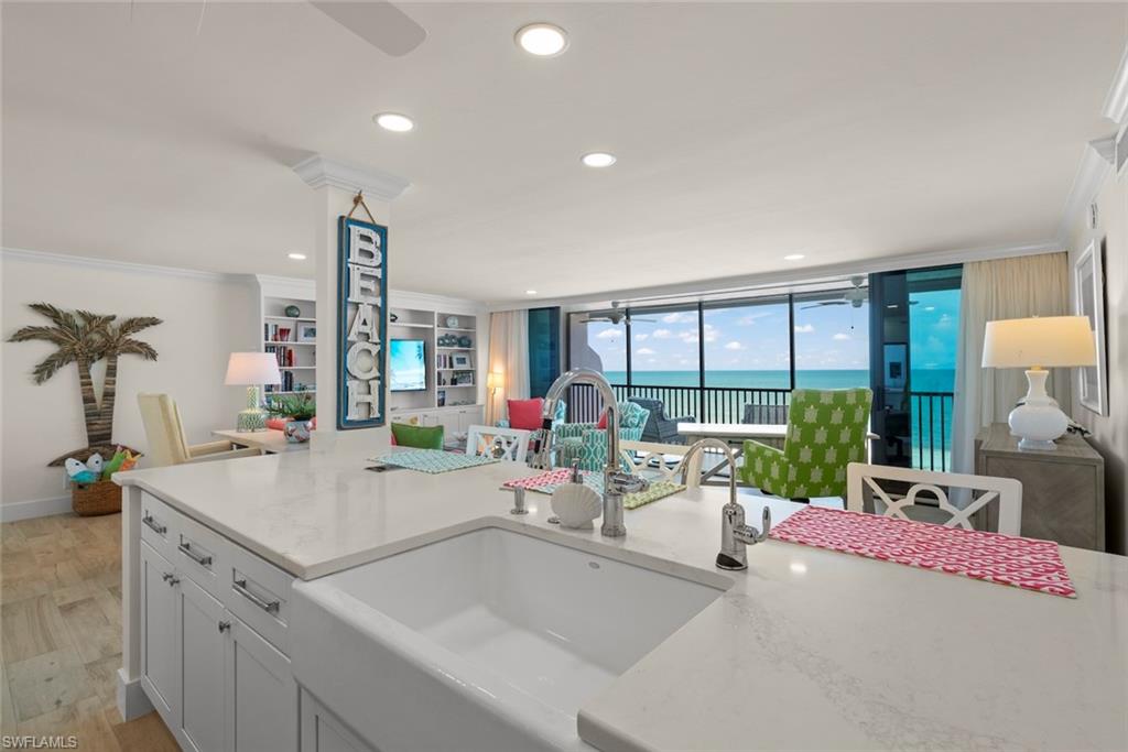 Kitchen island featuring a farmhouse sink and light-toned countertop, with open-concept living area and floor-to-ceiling sliding glass doors