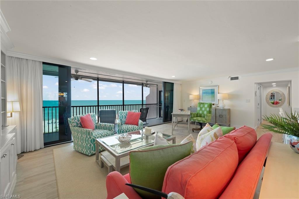 Living area featuring floor-to-ceiling sliding glass doors, light wood-finish flooring, a built-in wall unit with display shelving, recessed lighting, and direct access to an outdoor balcony with water views