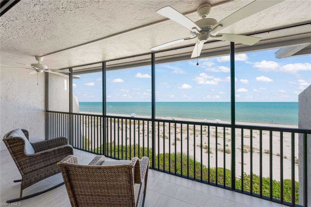 Screened balcony featuring expansive ocean and beach scenery, two ceiling fans, and light-toned tile flooring