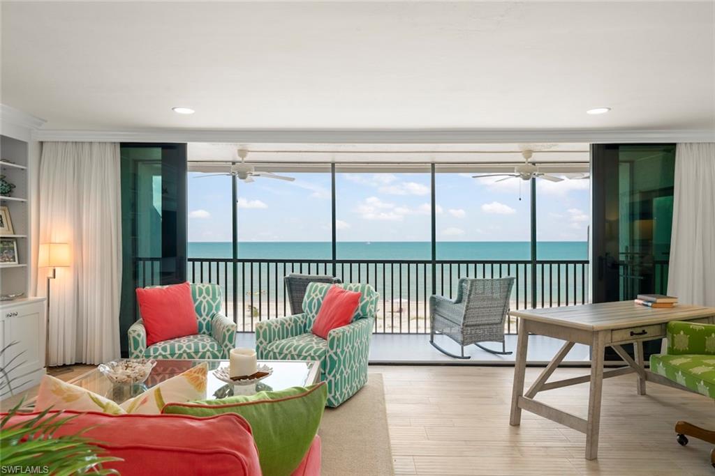 Living area featuring floor-to-ceiling sliding glass doors, light wood-finish flooring, a built-in wall unit with display shelving, recessed lighting, and direct access to an outdoor balcony with water views
