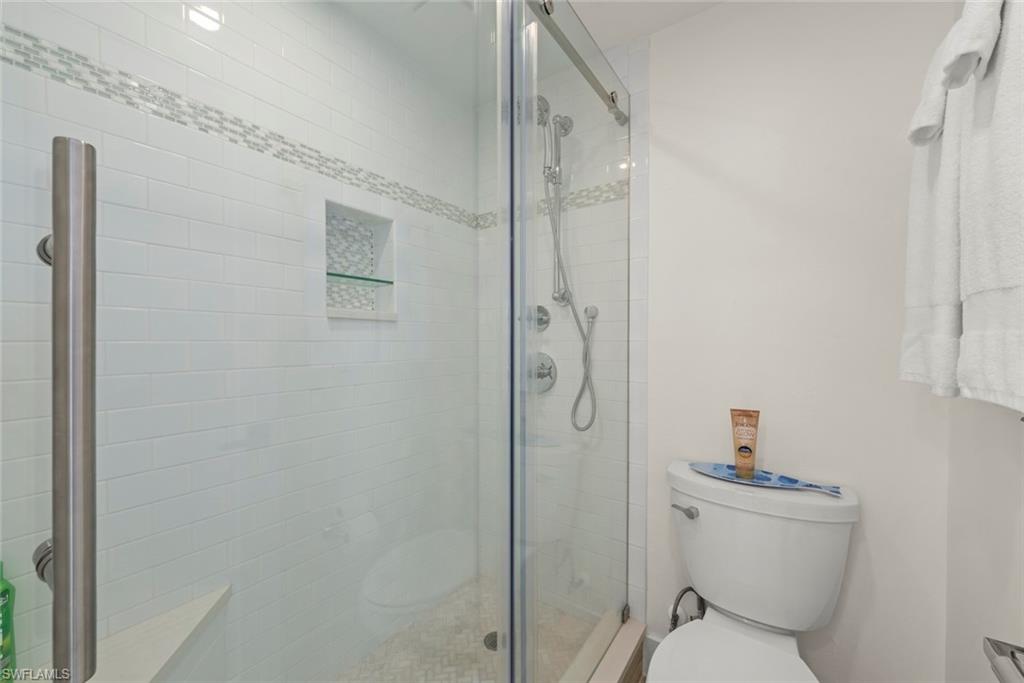 Glass-enclosed shower featuring white subway tile, a decorative mosaic tile accent band, and a built-in shower niche with a glass shelf