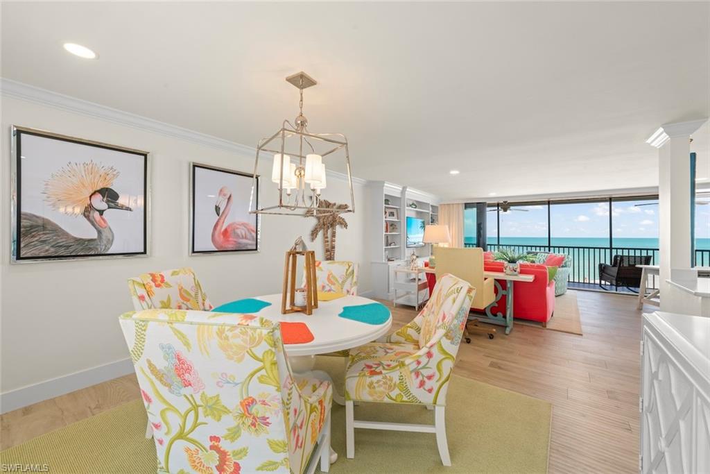 Open-concept living space featuring wood-finish flooring, built-in shelving, a full wall of glass overlooking the ocean, and a recessed ceiling with crown molding