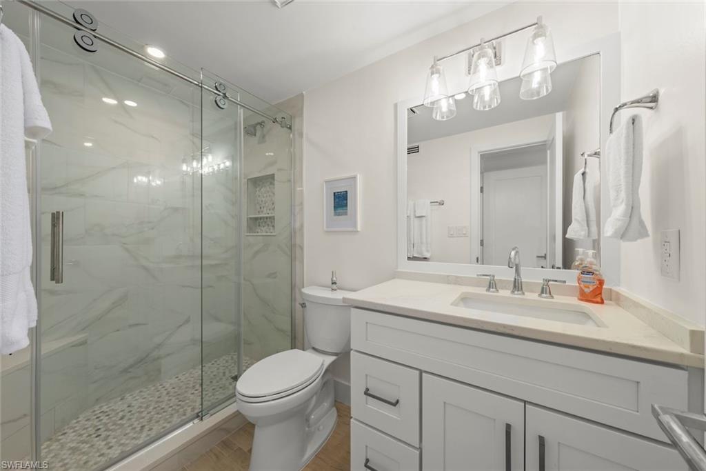 Bathroom featuring a walk-in shower with a glass sliding door, stone pebble floor, and marble-look tile surround
