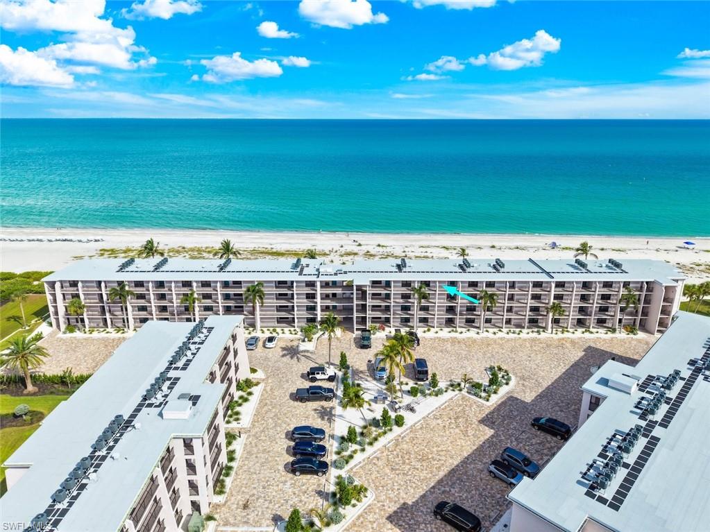 Coastal condominium building with direct beachfront access, featuring private balconies, mature palm trees, and a paver drive