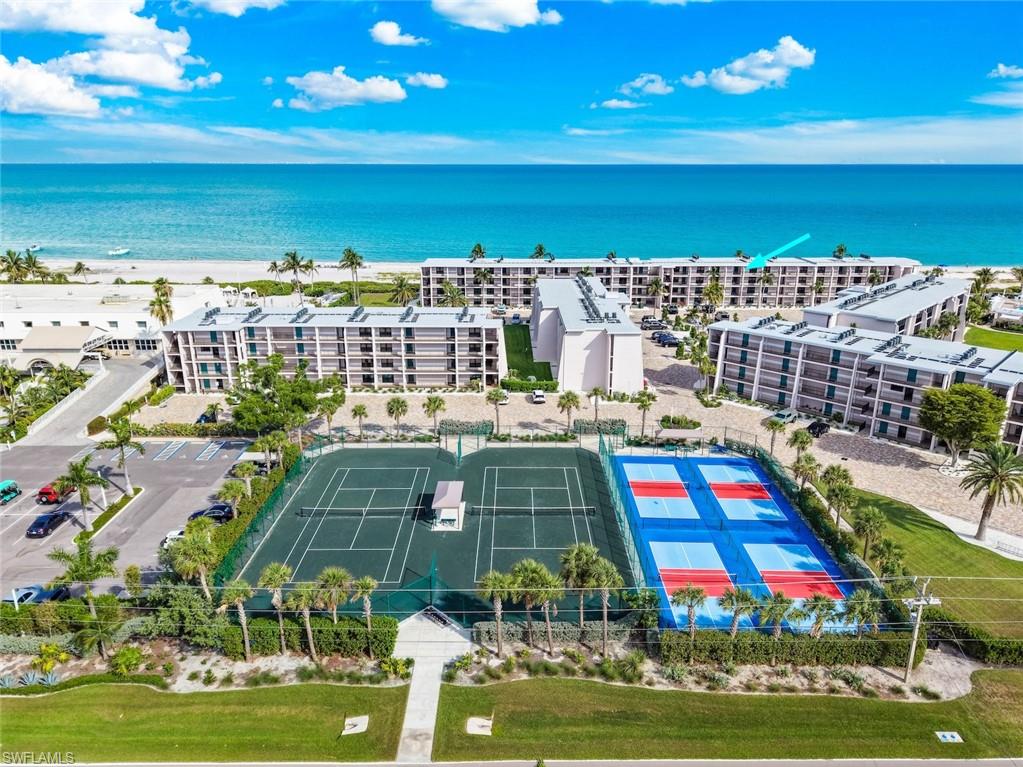 Coastal condominium complex featuring multiple buildings with balconies, tennis courts, and beachfront access to a sandy shoreline and the Gulf of Mexico