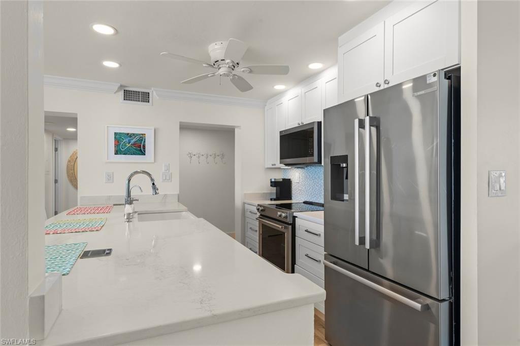 Modern kitchen featuring a large island with a sink, white shaker cabinetry, stainless steel appliances, and a tiled backsplash