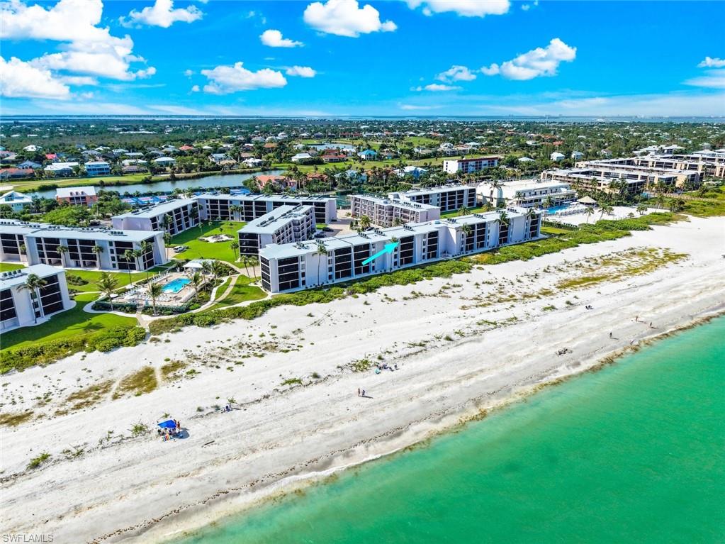 Beachfront condominium complex featuring multiple buildings with private balconies, manicured green spaces, and a communal swimming pool