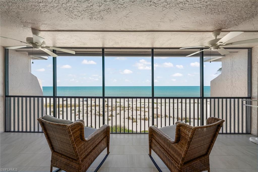 Screened balcony featuring direct beachfront exposure, tile flooring, and two ceiling fans