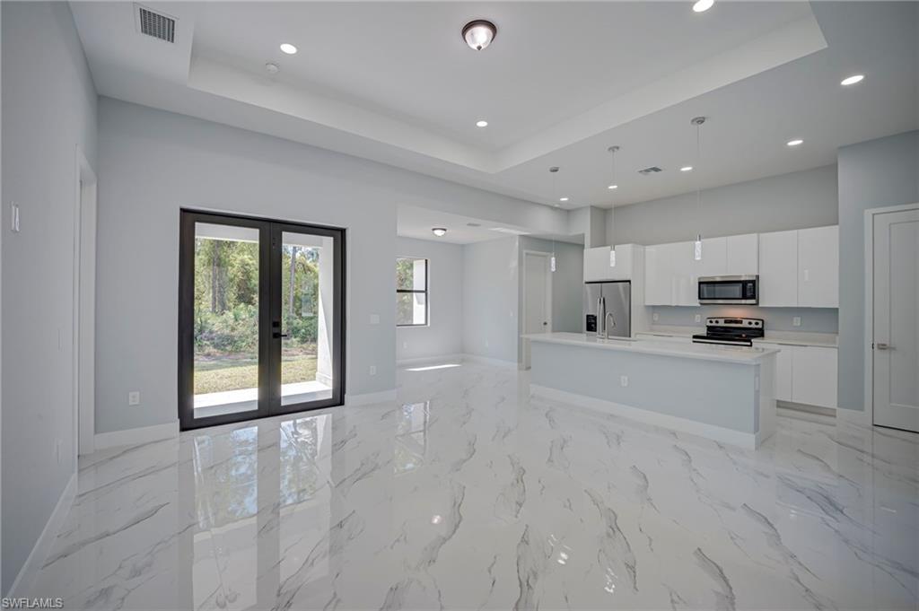 Kitchen featuring open floor plan, white cabinetry, an island with sink, french doors, and stainless steel appliances