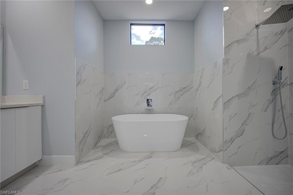 Bathroom with a marble finish shower, a freestanding tub, light marble finish floors, and vanity
