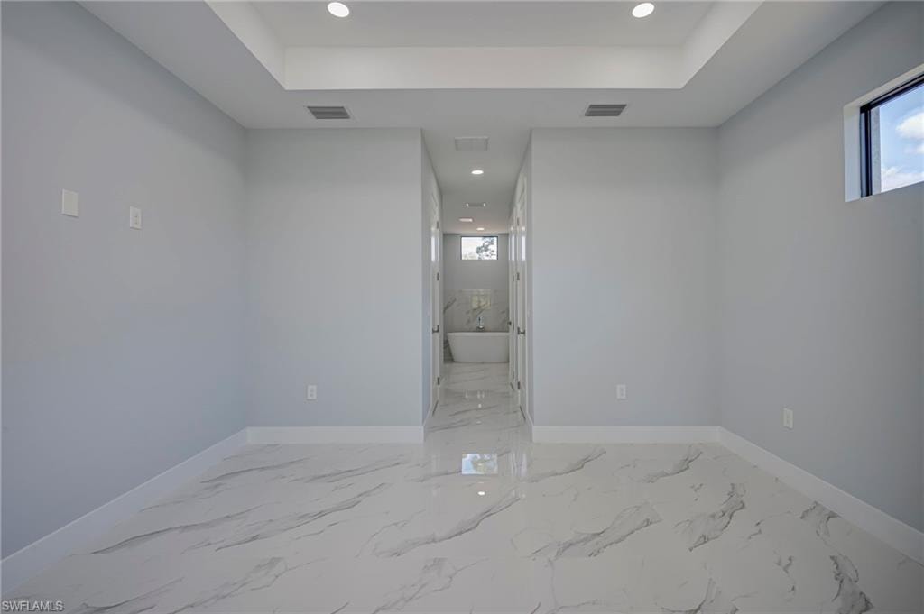 Unfurnished room featuring recessed lighting, light marble finish flooring, and a raised ceiling