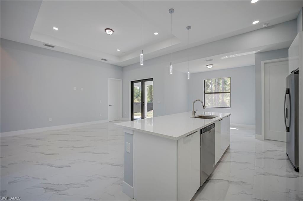 Kitchen featuring plenty of natural light, white cabinetry, a center island with sink, stainless steel appliances, and a tray ceiling