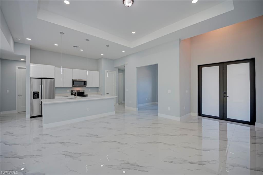 Kitchen with open floor plan, french doors, white cabinets, stainless steel appliances, and an island with sink