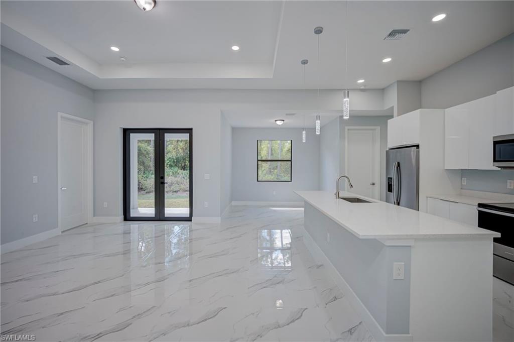 Kitchen with white cabinets, stainless steel appliances, open floor plan, french doors, and a kitchen island with sink