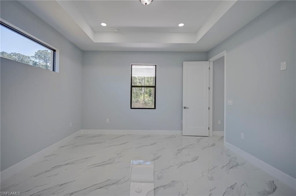 Spare room featuring light marble finish flooring, a raised ceiling, and recessed lighting