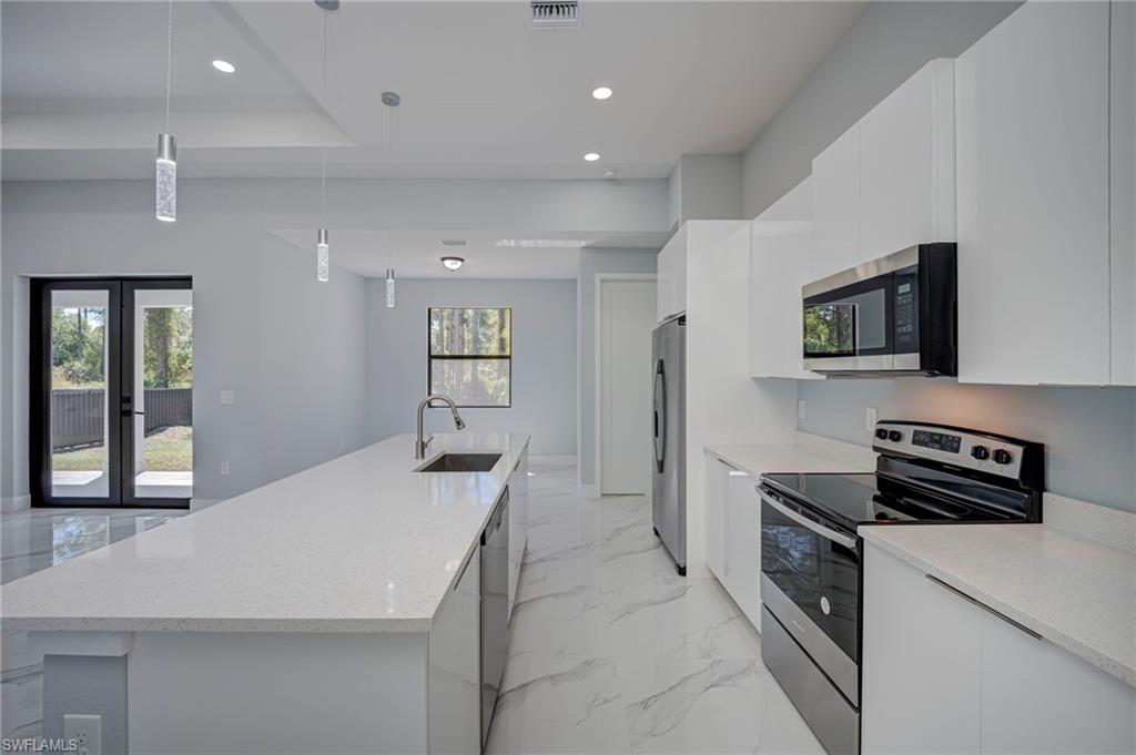 Kitchen with stainless steel appliances, a large island, light stone counters, white cabinetry, and hanging light fixtures