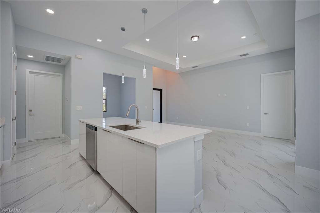 Kitchen with modern cabinets, white cabinets, light stone counters, hanging light fixtures, and a center island with sink
