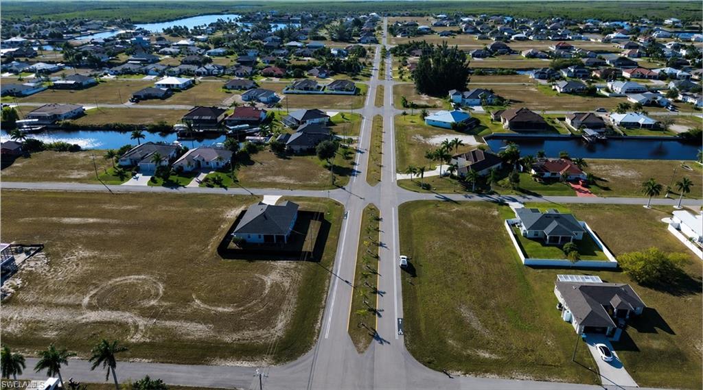 Expansive aerial capturing multiple single-story residences with diverse architectural styles, featuring paved roadways, individual driveways, and partially developed lots