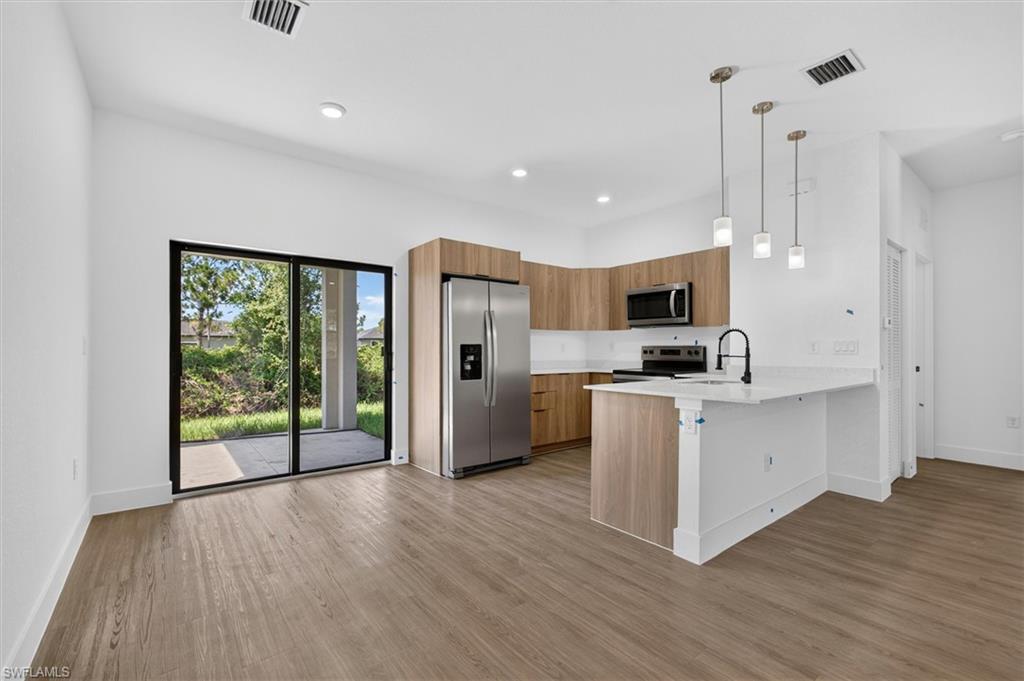 Open-concept kitchen with wood-finish cabinetry, stainless steel appliances, and a central island featuring a white countertop and pendant lighting