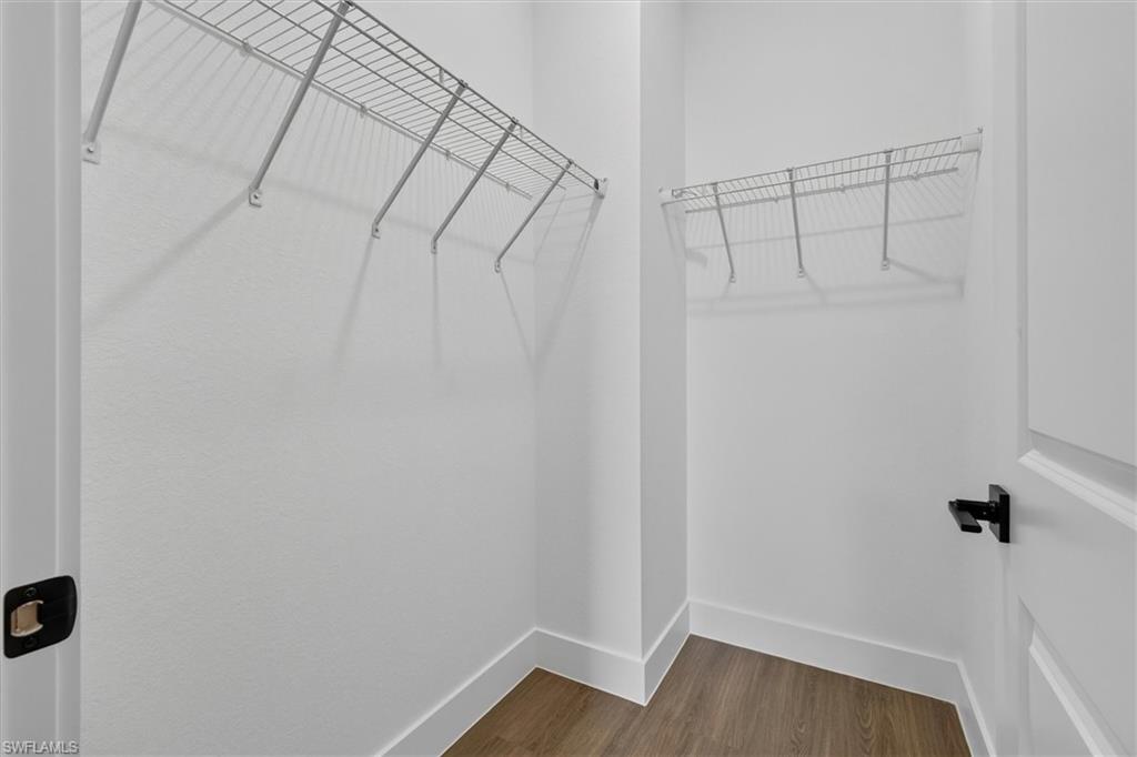 Walk-in closet featuring wire shelving, white walls, wood-finish flooring, and crisp white baseboards