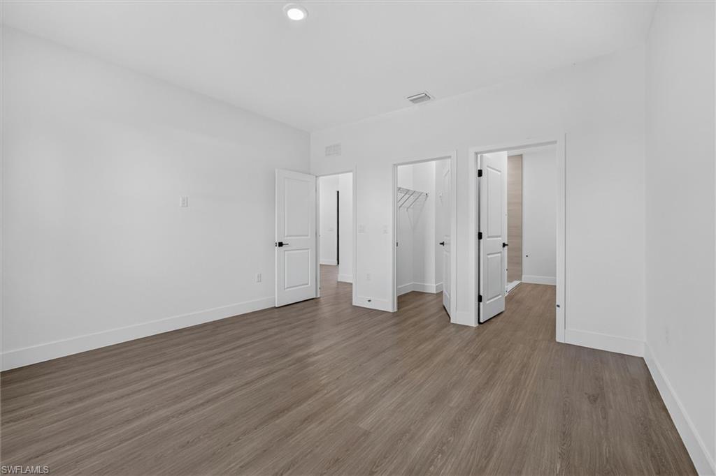 Spacious room featuring wood-finish flooring, white baseboards, and bright white walls