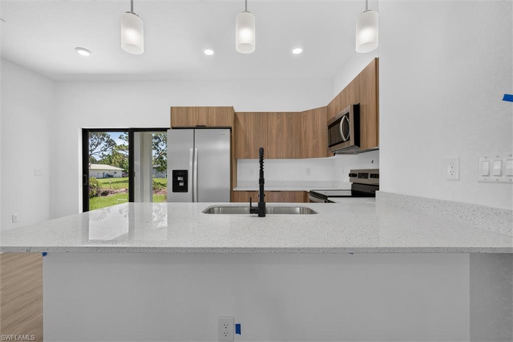 Kitchen featuring a large light-toned countertop, stainless steel appliances, wood-finish cabinetry, and recessed lighting