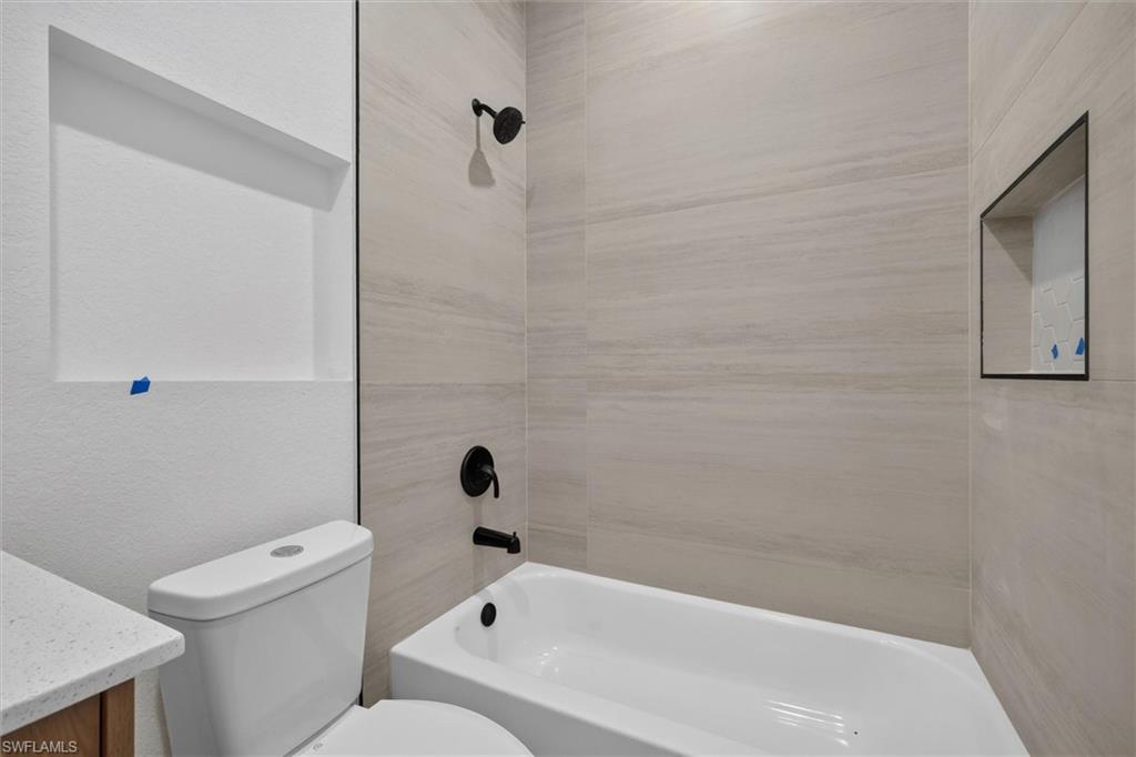 Contemporary bathroom featuring a white porcelain tub, matte black shower fixtures, a tiled shower surround, and a recessed shower niche
