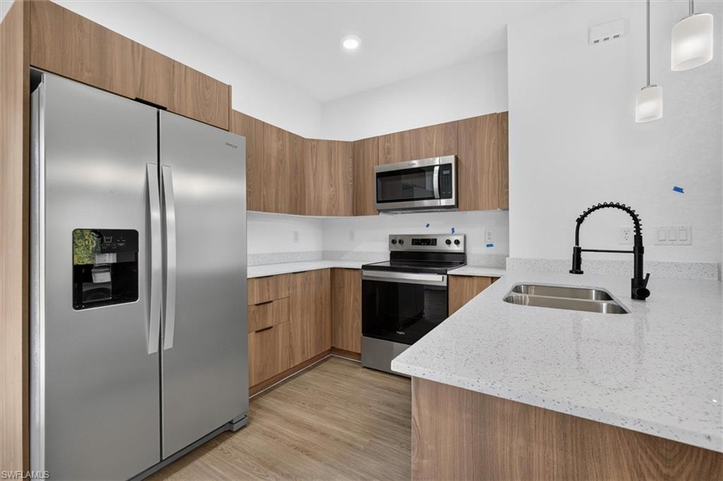 Contemporary kitchen with wood-finish cabinetry, white solid-surface countertops, and stainless steel appliances