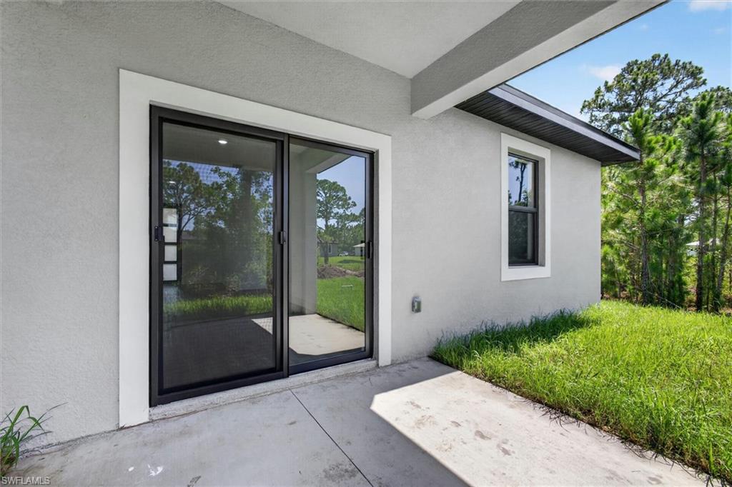 Outdoor patio space featuring a concrete surface, sliding glass doors, a single window with dark framing, a light-colored stucco exterior, and a black soffit