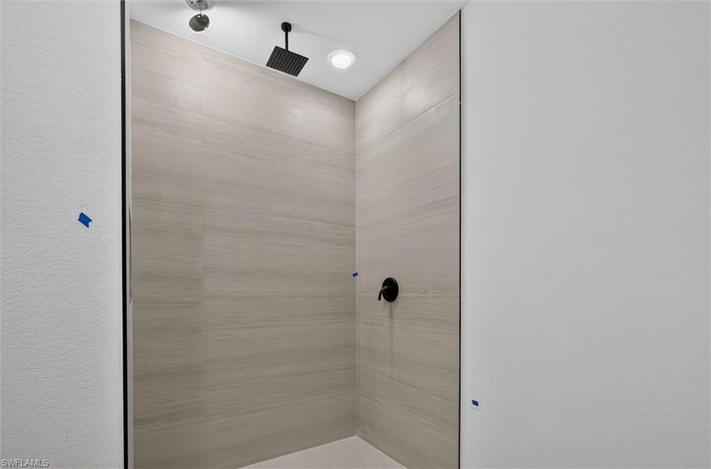 Shower enclosure featuring large format light-toned tile, a matte black rain shower head, and a coordinating matte black control knob