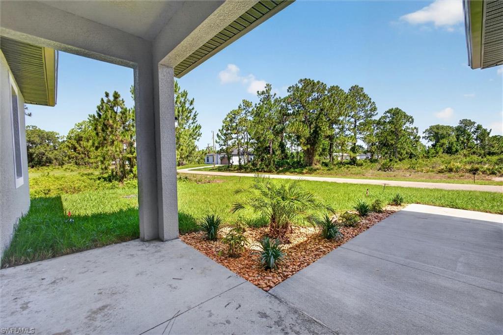 Concrete front porch with stucco columns, featuring a landscaped bed with a young palm and ground cover