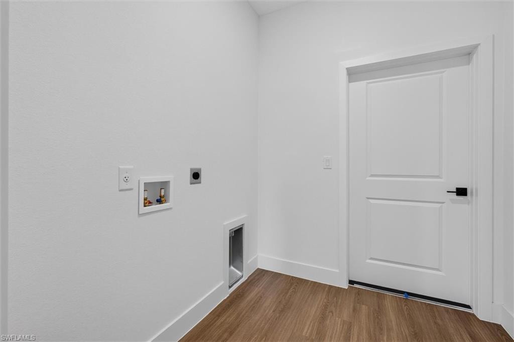 Dedicated laundry area featuring white walls, wood-finish flooring, and a paneled door with a matte black handle
