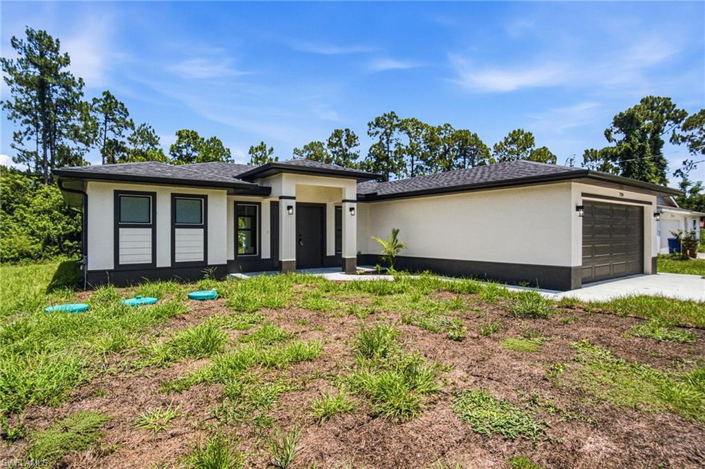 Contemporary exterior featuring a neutral stucco finish, dark trim accents, a prominent covered entry, and a two-car garage