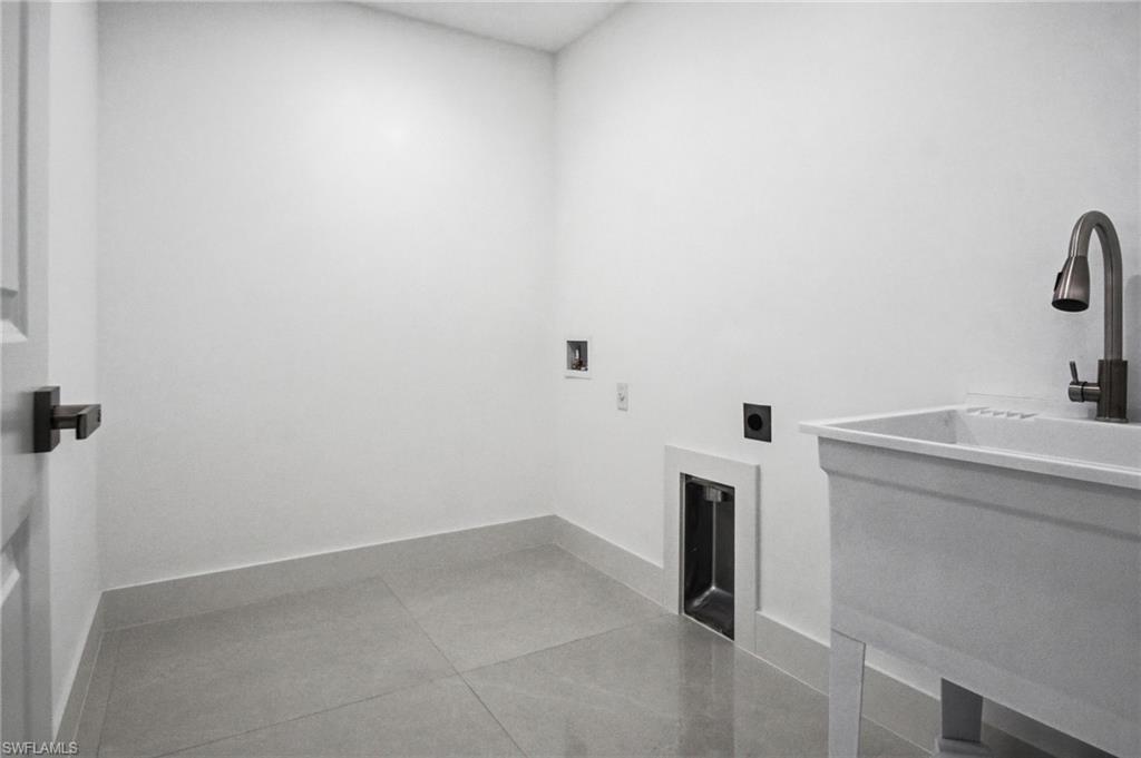 Dedicated laundry room featuring light gray floor tiles, a utility sink with a gooseneck faucet, and white baseboards