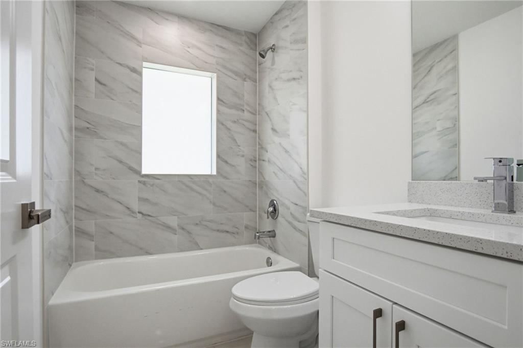 Bathroom featuring a white tub, shower with large format tile surround, vanity with stone countertop, and an integrated rectangular sink