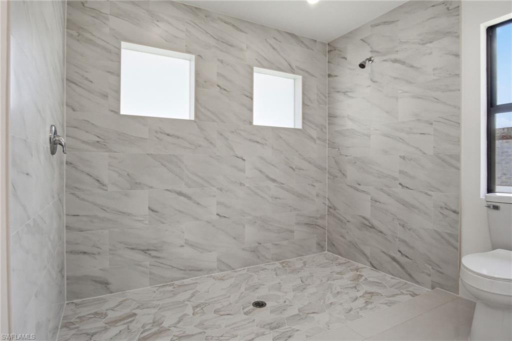 Walk-in shower featuring large format marbled tile walls, mosaic tile flooring, a chrome showerhead, and two frosted windows