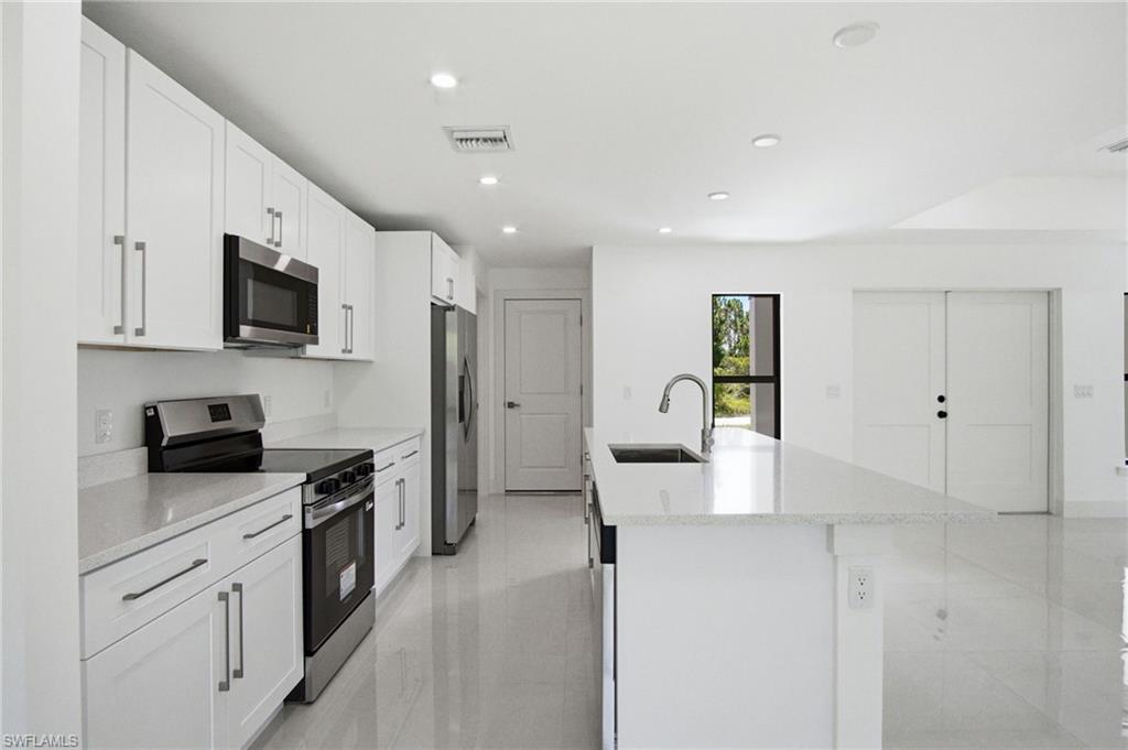 Modern kitchen featuring white cabinetry with brushed nickel hardware, stainless steel appliances, a center island with a sink and gooseneck faucet, light-toned countertops, and recessed lighting