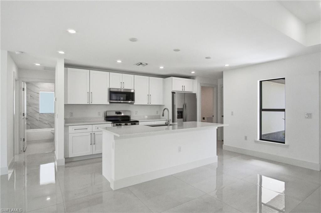 Bright kitchen featuring white cabinetry, stainless steel appliances, a center island with sink, and recessed lighting