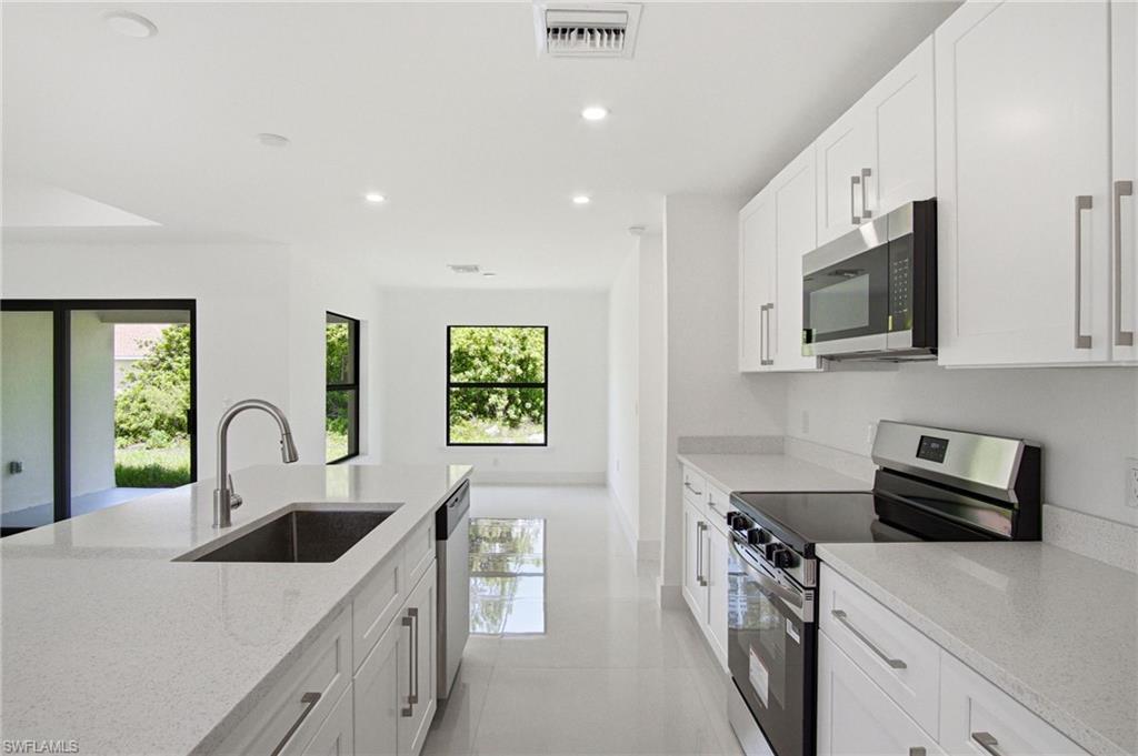 Modern kitchen featuring white shaker cabinetry, stainless steel appliances, light-toned countertops, a kitchen island with an undermount sink, and recessed lighting
