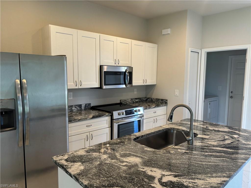 Kitchen with white cabinets, sink, dark stone countertops, and stainless steel appliances