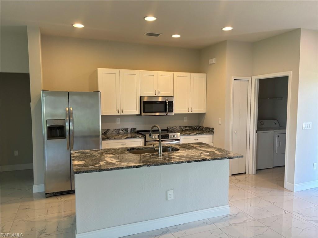 Kitchen featuring dark stone counters, a kitchen island with sink, washer and dryer, appliances with stainless steel finishes, and sink